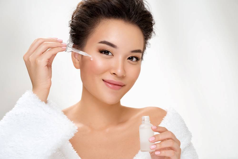 Asian woman applying serum to her face